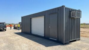 Customized shipping container office with a roll-up door and AC unit on a construction site
