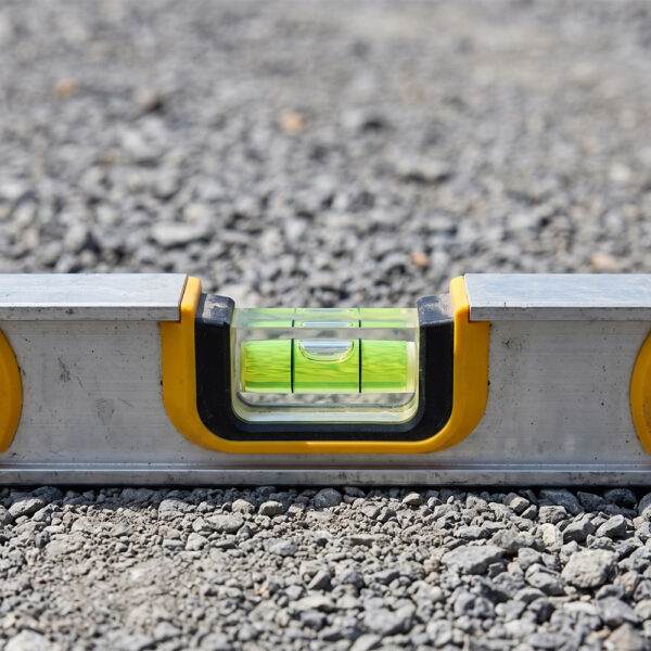 A close-up view of a builder's spirit level resting perfectly even on compacted road base gravel, demonstrating a level foundation.