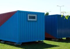 two blue shipping containers sitting on concrete blocks surrounded by grass