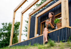 woman sits under a pergola outside of a modern structure